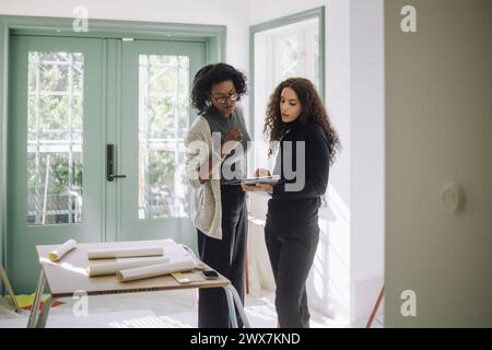 Architect discussing with female client over digital tablet while standing at under construction apartment Stock Photo