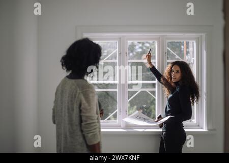 Side view of female construction engineer talking to client while standing near window at under construction apartment Stock Photo