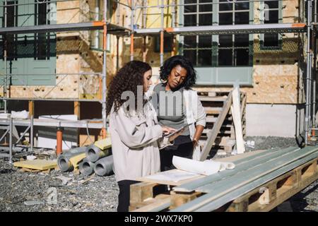 Female construction engineer discussing with client over digital table while standing in front of under construction apa Stock Photo