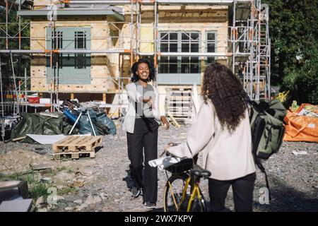 Smiling customer greeting female architect arriving with bicycle at construction site Stock Photo