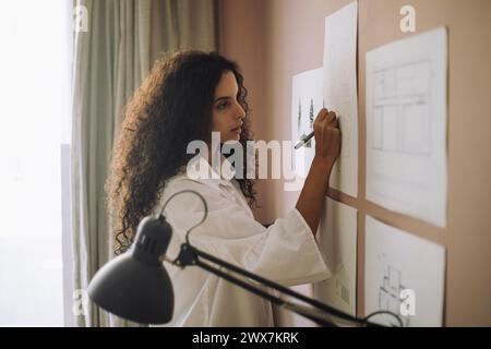 Focused female architect preparing blueprints on paper while working at office Stock Photo