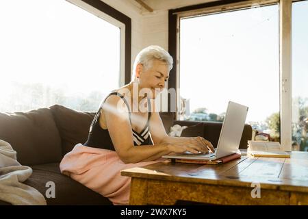 Senior woman using laptop while sitting on sofa at houseboat Stock Photo