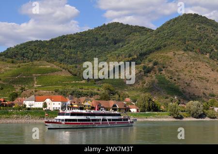 A river cruise ship sails past the town of Spitz and its terraced vineyards along the Danube River in Lower Austria's scenic Wachau Valley. Stock Photo