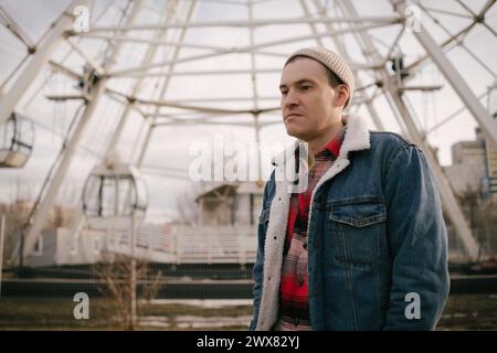 Man Standing in Front of Ferris Wheel. A man stands in front of a large ferris wheel at an amusement park. Stock Photo