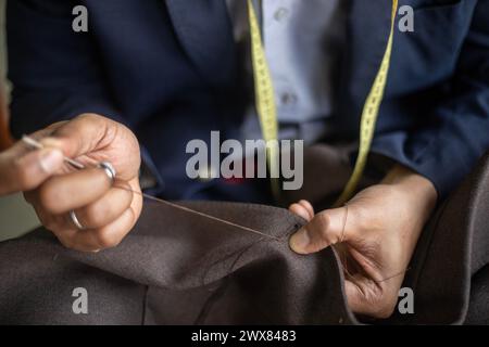 Detailed close up photo of a young African American tailor hand stitching the buttonhole of a bespoke jacket while super focused on the job Stock Photo