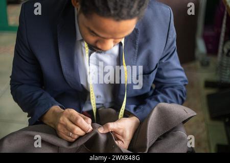 Detailed close up photo of a young African American tailor hand stitching the buttonhole of a bespoke jacket while super focused on the job Stock Photo