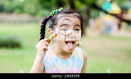 A young girl holds a toothbrush while peering through a magnifying glass Stock Photo