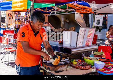 A Man Slicing Bread and Cooking Meat On A Barbeque In The Street In The La Boca District of Buenos Aires, Argentina. Stock Photo