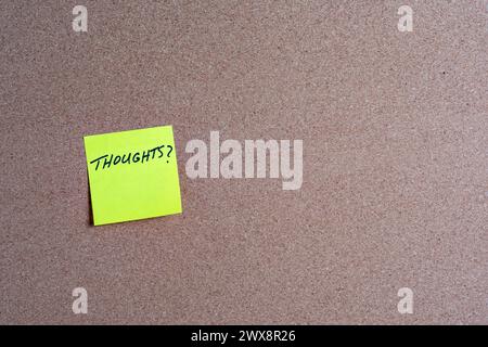 The word Thoughts on a yellow sticky note posted on a corkboard Stock Photo