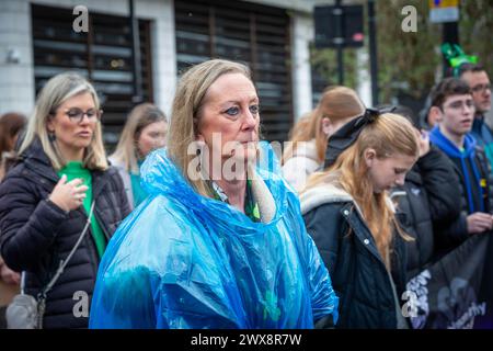 Unhappy lady in disposable poncho joins a procession in Warrington Town Centre for St Patrick's Day Stock Photo
