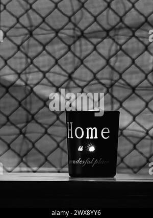 Engraved illumination. Candlelight in black glass, home wonderful place engraved message against wired diamond shaped interior background. Monochrome Stock Photo