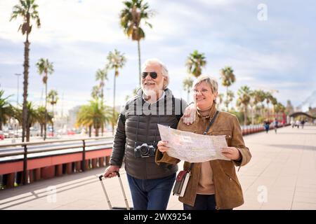 Couple of old Caucasian tourist walking hugging each other with their luggage facing forward Stock Photo