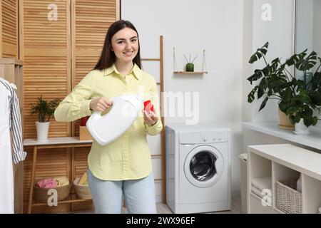 Beautiful young woman pouring detergent into cap in laundry room Stock Photo