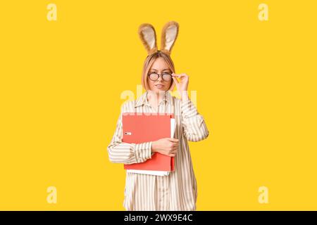 Adult female secretary in bunny ears with documents folder on yellow background. Easter celebration Stock Photo