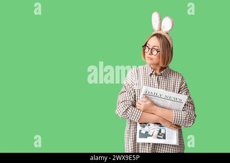 Adult female manager in bunny ears with newspaper on green background. Easter celebration Stock Photo