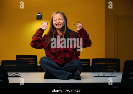 Young angry female IT employee with dog paw model gesticulating sitting on desk Stock Photo