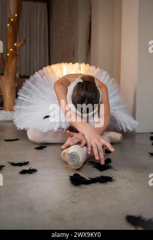 Ballerina portrays dying swan in the Swan Lake Ballet. Ballet dancer in pointe shoes lies on the floor among black fallen feathers. Talented theater a Stock Photo