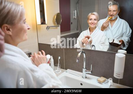 Woman with cream and man with croissants looking at themselves in mirror Stock Photo