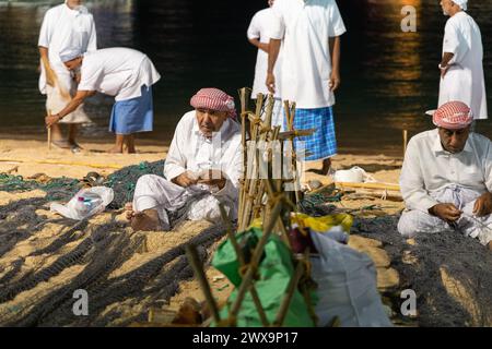An Arab man repairs a fishing net during the Katara International Dhow Festival in katara cultural village beach. Stock Photo