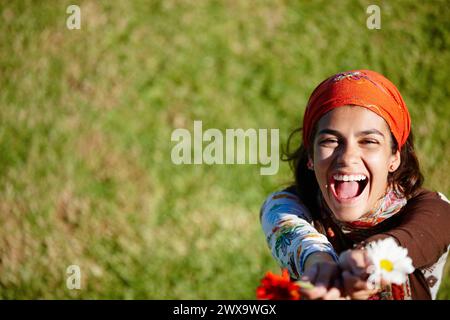 Woman, laugh and portrait for gypsy with flower in nature for summer, outdoor and adventure on grass. Young person, excited and bohemian style with Stock Photo