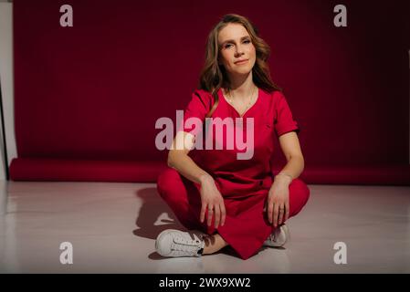 Young female nurse in a pink uniform sitting on the floor on a pink background Stock Photo