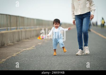 infant baby learn walking first step on a pathway with mother helping Stock Photo
