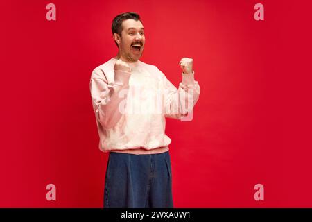 Man, sport fan expressing happiness and joy, celebrating victory isolated on red studio background. Excitement, expressive positive face Stock Photo