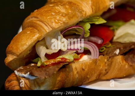 Image of onion rings, lettuce and tomatoes in a croissant with meat and sauce Stock Photo