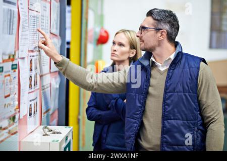 People, planning and checking schedule with board in warehouse with calendar for order details. Man, woman and together with checklist or clipboard Stock Photo