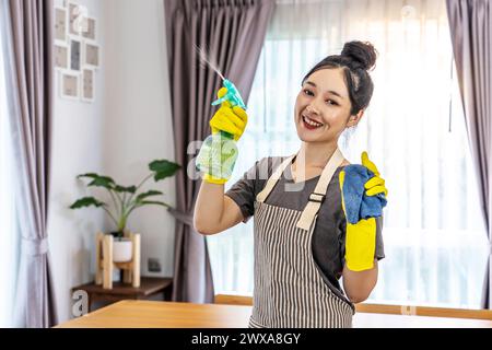 A Southeast Asian woman with cleaning supplies in hand poses for the camera Stock Photo