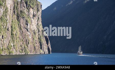 Tourist sightseeing boat sailing through fjord with steep rocky wall, Fiordland, New Zealand. Stock Photo