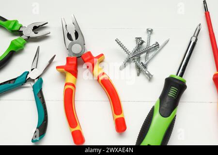Pliers, screwdrivers and screws on white wooden table, flat lay Stock Photo