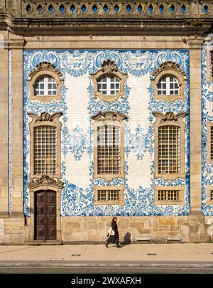 Woman passes by the facade of Igreja do Carmo church, adorned with intricate blue and white tiles, Porto, Portugal Stock Photo