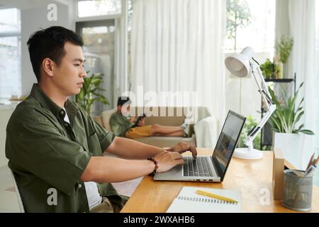 Serious man working on laptop at home when his son drawing on tablet in background Stock Photo