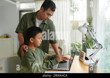 Father helping preteen son working on laptop Stock Photo