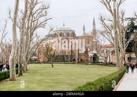 Historic Hagia Sophia mosque exterior with its large dome and minarets surrounded by leafless trees and a green lawn Stock Photo