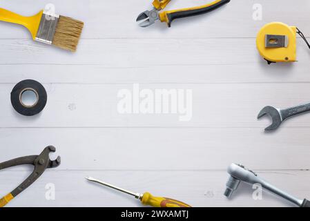 Top view of assorted tools neatly arranged on a white wooden desk, with copy space in the center. Flat lay composition ideal for DIY concept promotion Stock Photo