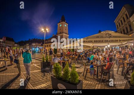 BRASOV, ROMANIA - JULY 11, 2020: Night view of the Council Square with tourists, located in the historic centre of the City. It is surrounded by 18th- Stock Photo