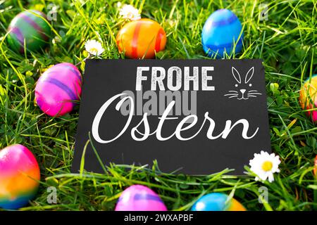 March 29, 2024: Happy Easter Greetings on a board in a green meadow with colored Easter eggs. Greetings for Easter. PHOTOMONTAGE *** Frohe Ostern Grüße auf einer Tafel in einer grünen Wiese mit gefärbten Ostereiern. Gruß zu Ostern. FOTOMONTAGE Stock Photo