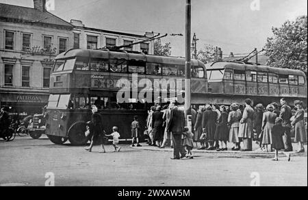 A busy scene at the bus stop at The Bridge in Walsall, West Midlands, England, UK c. 1950. The long queue has formed, waiting for a trolleybus to take them to Bloxwich. Trolleybus 155 (centre left) was a Sunbeam MS2 and entered service in 1933. It was retired in 1951.Walsall town centre had many stores including Pattisons, a cake shop (left). This is taken from an old photograph album – a vintage 1940s/50s photograph. Stock Photo