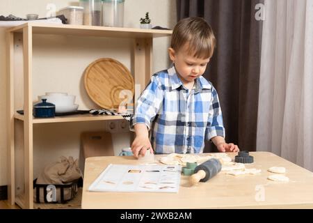 Two-year-old boy making his first cookie with a recipe book for toddlers Stock Photo