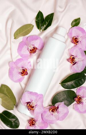 Ecological laundry detergent among orchid flowers on bed linen top view Stock Photo