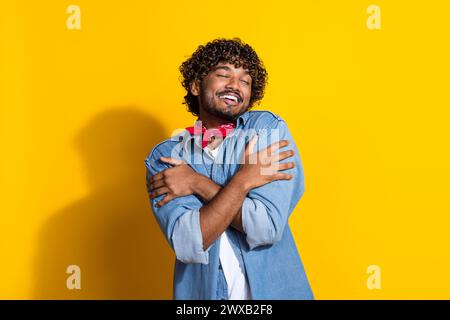 Photo portrait of handsome young guy cuddle self shoulders wear trendy denim garment red scarf isolated on yellow color background Stock Photo