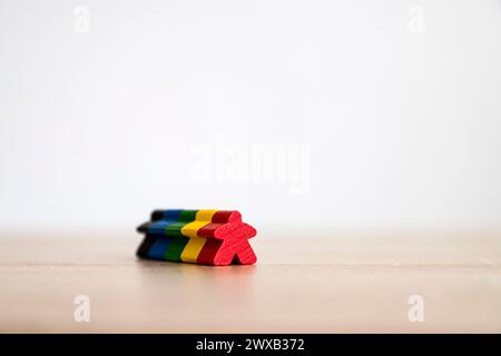 A single red wooden figure lies on a table surface with multicolored wooden shapes in the background. Stock Photo