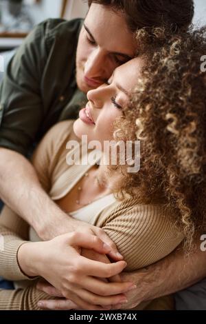 Closeup photo of curly young woman and brunette man sharing a heartfelt hug in bedroom Stock Photo