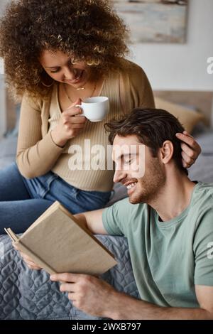curly young woman and brunette man engage in lively talk over coffee, book in his hands Stock Photo