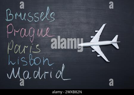 Traveling concept. Toy plane over chalkboard with cities written on it Stock Photo