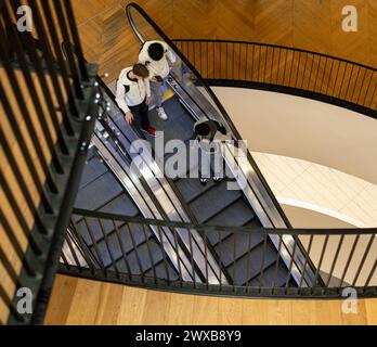 View from above of three young men on escalator in multiple floored Birmingham City Library.  Gallery railings at different levels and view through. Stock Photo