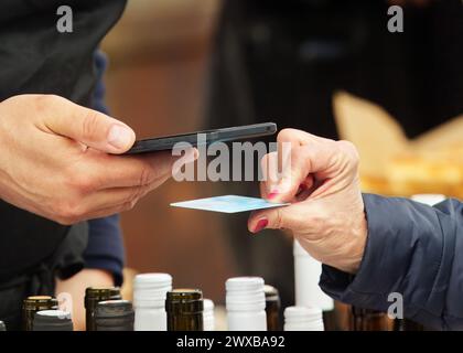 Outstretched hand of vendor holding terminal for electronic  payment and hand of customer holding credit card at the farmers street food market at Pra Stock Photo