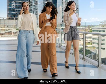 Three businesswomen are walking while using smartphones Stock Photo